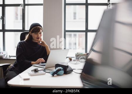 Female entrepreneur working on laptop while sitting at desk in office Stock Photo
