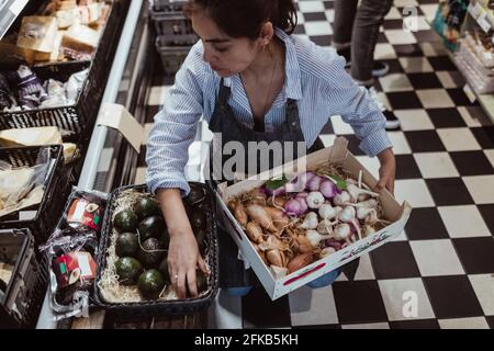 High angle view of sales woman arranging fruits and vegetables in box at deli store Stock Photo
