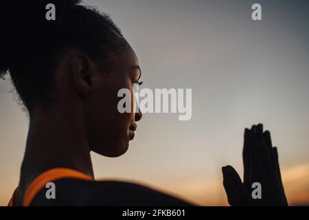 Young sportswoman practicing yoga against sky during sunset Stock Photo