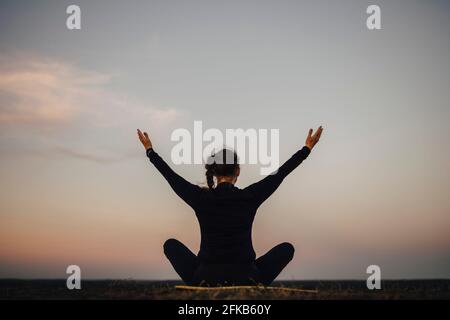 Rear view of sportswoman practicing yoga against sky during sunset Stock Photo