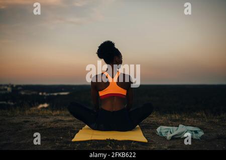 Rear view of sportswoman sitting on exercise mat during sunset Stock Photo