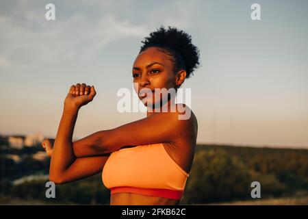 Female athlete doing stretching exercise against sky during sunset Stock Photo