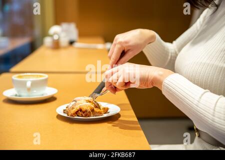 woman cuts croissant and drinks coffee at a table in a cafe. no face Stock Photo