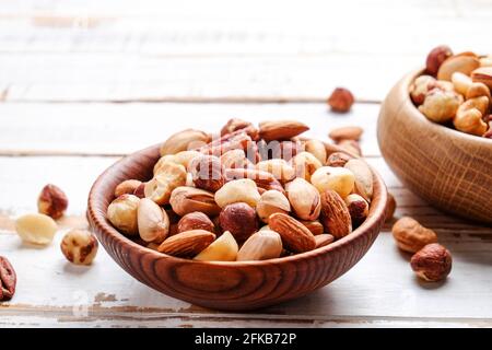 Mixed nuts in wooden bowl and scattered on table. Trail mix of pecan, almond, macadamia & brazil edible nuts with walnut hazelnut on wood textured sur Stock Photo