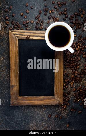 Empty black frame with White cup of black coffee and coffee beans on dark concrete background. The concept of hot drinks,  Invigorating breakfast. cop Stock Photo