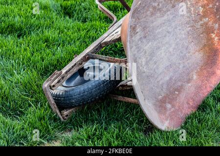 Closeup of rusty metal wheelbarrow lying sideways in the grass Stock Photo