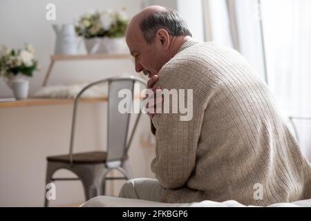 Senior man with osteoarthritis pain holding hand on his shoulder sitting at home Stock Photo
