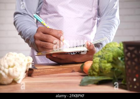 young man writing diet pan on notepad on kitchen table  Stock Photo