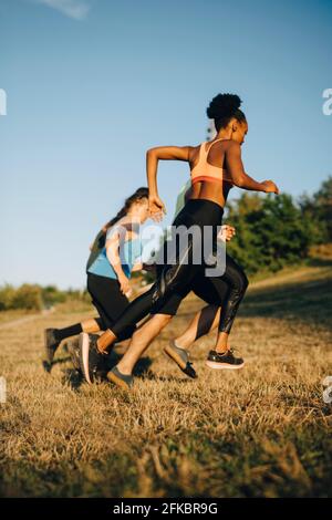 Male and female athletes running on grass against sky in park Stock Photo