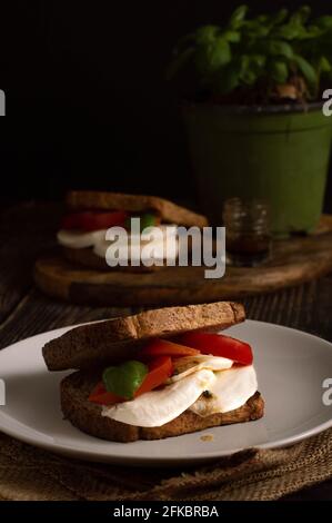 Italian tomato and mozzarella cheese sandwich (also called 'caprese sandwich'). Wooden background, a basil plant on the back. Olive oil on the top of Stock Photo
