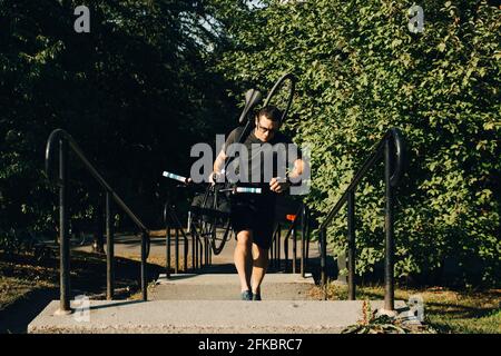 Active male athlete climbing steps while carrying bicycle in park Stock Photo