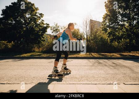 Female athlete roller skating on street during sunny day Stock Photo