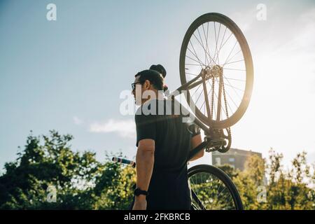 Male athlete carrying bicycle on shoulder against sky on sunny day Stock Photo