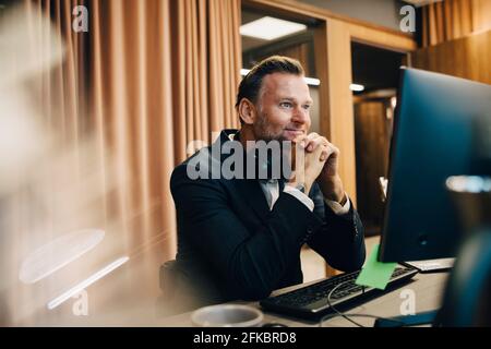 Smiling male entrepreneur with hand on chin working over laptop in office Stock Photo