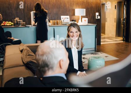 Smiling female entrepreneur discussing with male colleague in cafeteria at office Stock Photo