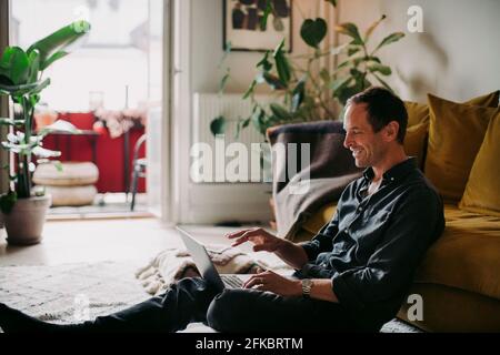 Businessman laughing while working on laptop in living room at home Stock Photo