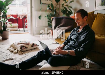 Smiling businessman working on laptop in living room Stock Photo