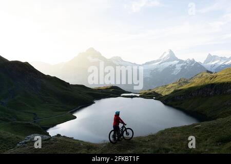 Hiker with mountain bike admiring sunrise over Bachalpsee lake, Grindelwald, Bernese Oberland, Bern Canton, Switzerland, Europe