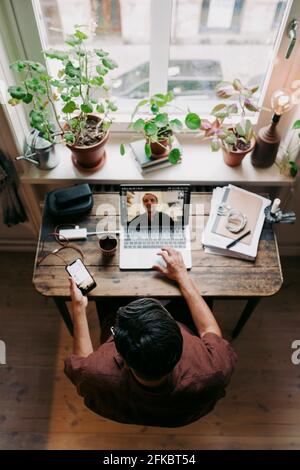 Businessman using smart phone while discussing with colleague on video call at home office Stock Photo