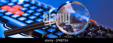 Magnifying glass on the keys of a black computer keyboard. Stock Photo