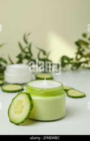 Jars with cosmetic cream, cucumber slices and branch on white table Stock Photo