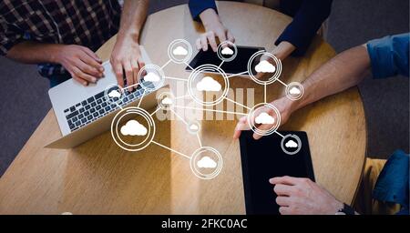 Connected network of bubbles with cloud icons over businessmen at table with laptop and tablets Stock Photo