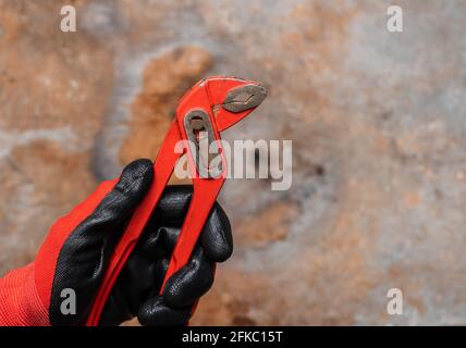 Mechanic or plumber wearing protective glove holding red adjustable pliers against rusty metal background Stock Photo