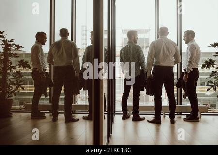 Business people discussing with each other while standing in front of window at office Stock Photo