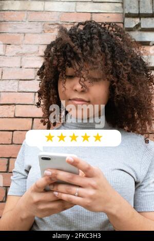 Curly-haired girl using a smartphone to rate a service experience with five stars. Business concept. Stock Photo