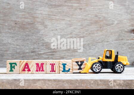 Toy bulldozer hold letter block y to complete word family on wood background Stock Photo