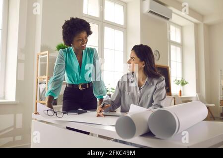 Diverse young multiethnic woman architects discussing blueprints in office Stock Photo