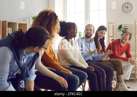Interracial people sit in a row and communicate with each other sharing experiences. Stock Photo