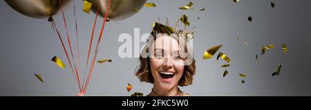 happy plus size woman in crown holding balloons near confetti on grey, banner Stock Photo