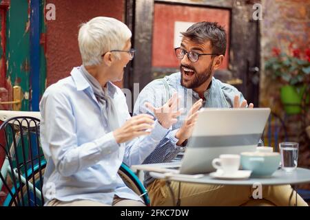 An elderly woman has an interesting talk with her young male friend while spending free time at bar's garden together on a beautiful day. Leisure, bar Stock Photo
