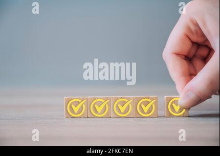 Checklist concept, yellow check mark on wooden blocks on wood background with copy space. Hand holding wooden blocks with check marks. Stock Photo