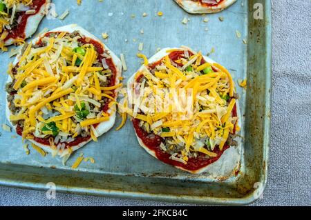 The crust has been prepared, sauce applied, hamburger meat piled on and lots of shredded cheese added to the top. These little pizzas are ready to go Stock Photo