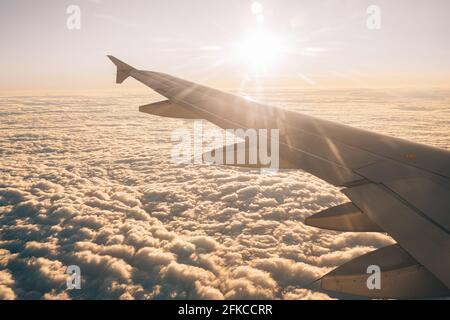 Sun shines brightly on the clouds under the wing of the plane. View from the porthole Stock Photo