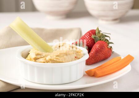 Celery stick dipped in hummus with carrots and strawberries on the side. Stock Photo