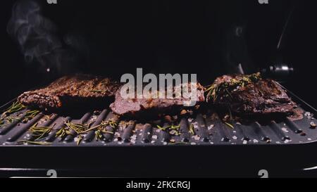 Delicious juicy meat steak cooking on grill. Prime beef fry on electric roaster, rosemary, black pepper, salt. Slow motion. Stock Photo