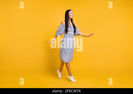 Photo of impressed cute young lady wear striped clothes walking looking empty space isolated yellow color background Stock Photo