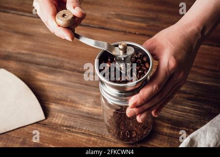 Grinding coffee beans in a manual coffee grinder on a wooden table Stock Photo