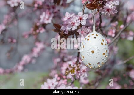 Decorative Easter egg hanging on flowering cherry tree with pink flowers. Easter background. Blossoms on a sunny spring day. Selective focus Stock Photo