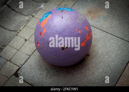 Close up high angle view image of a Colorful concrete ball on dull grey pavement, with worn out colorful layers of paint. Stock Photo