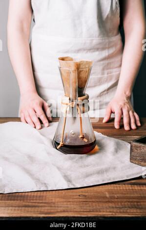 Closed up view of a manual glass coffee pot with filter and freshly brewed coffee inside on a wooden table Stock Photo