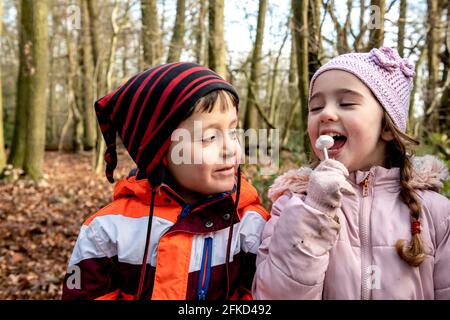 UK, Smiling boy looking at girl eating lollipop in Autumn park Stock Photo