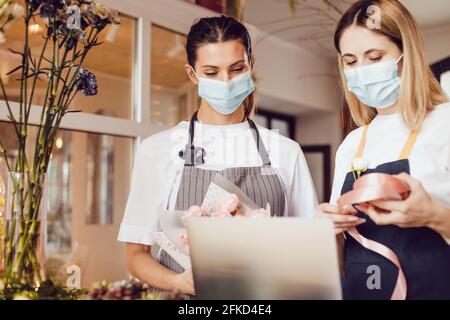 Flower shop workers in protective masks decorate a bouquet and use a laptop. Stock Photo
