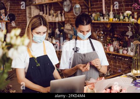 Flower shop workers in protective masks using laptop. Stock Photo