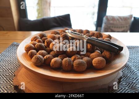 Closeup view of a bunch of walnuts on a white plate with a metallic nut cutter. The plate is placed on a wooden table in a cozy room. Zakopane, Poland. Cushions in the background.  Stock Photo