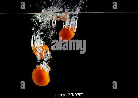 three tangerines fall into the water on a black background Stock Photo