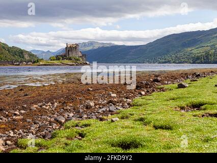 A castle on top of a grass covered field with Eilean Donan in the background Stock Photo